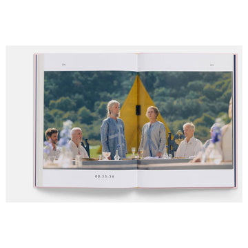 Open book showing a scene with people at a table outdoors, with a yellow tent in the background.
